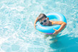 Cute baby boy in white sunglasses swimming with a blue inflatable ring in the clear water of the pool	
