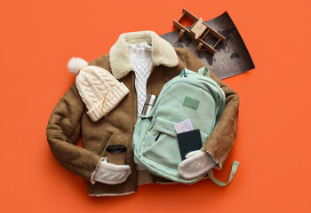 Sticker - Backpack with warm clothes, world map, passport and cup of coffee on orange background. Winter vacation concept