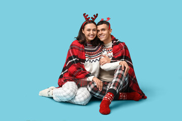 Canvas Print - Happy young couple in Christmas pajamas and with plaid sitting against blue background