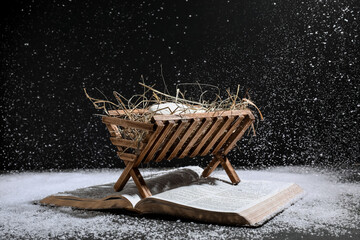 Wall Mural - Bible and wooden manger with dummy of baby on black background. Concept of Christmas story