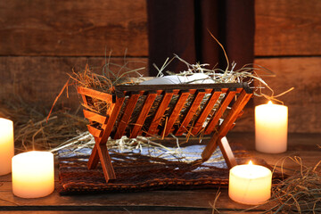 Wall Mural - Burning candles and manger with dummy of baby on brown wooden background. Concept of Christmas story