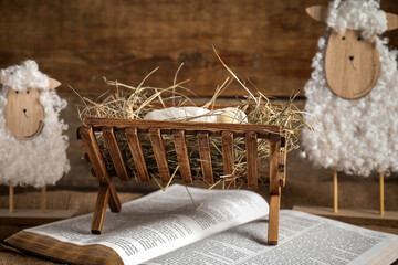 Bible, toy sheep and manger with dummy of baby on brown wooden background. Concept of Christmas story