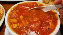 Stirs Red Chili Soup In A White Plate With A White Spoon