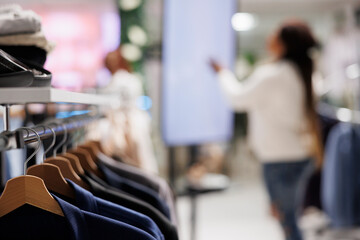 Wall Mural - Stylish clothes hanging on rack in shopping mall with blurred background. Trendy jackets on hangers showcasing merchandise brand new collection in fashion boutique close up