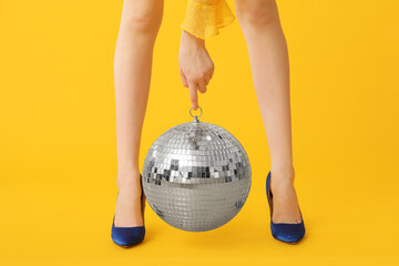 Wall Mural - Female legs in trendy high heels with disco ball on yellow background