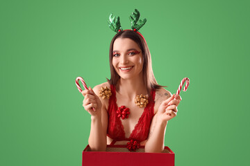 Poster - Beautiful young happy woman in Christmas deer horns with gift box, bows and candy canes on green background