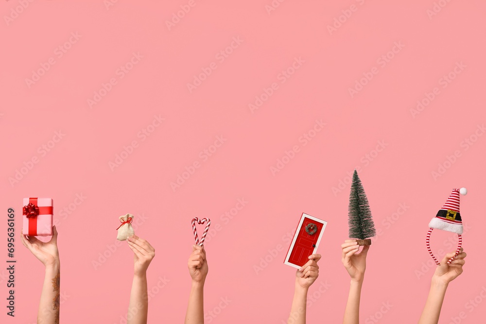 Female hands with Christmas fir tree, elf hat and gift box on pink background