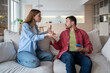 © DimaBerlin - Distrustful jealous woman asks husband to show cellphone trying to talk sitting on couch at home. Claim quarrel misunderstanding in neurotic couple relationship. Marital discord, family conflict.