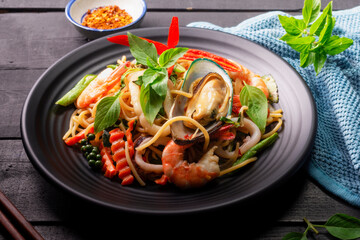 Canvas Print - Seafood drunken spaghetti with shrimp squid clams chili, and basil. Thai food. Healthy Asian in a plate on a black background table. Top view.