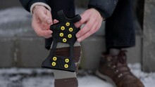 Hands Putting Ice Spikes On Slippery Shoes For Better Grip On Ice, Close Up