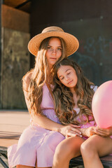 Wall Mural - Portrait of mother and daughter in pink dresses with flowing long hair against the black backdrop. The woman hugs and presses the girl to her.