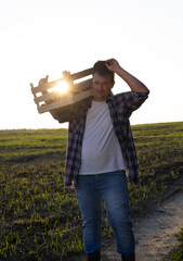 Wall Mural - vertically. A farmer with a box of potatoes stands in a field against the backdrop of a beautiful sunset. The concept of agriculture and small business Farmer at the end of the day after the harvest.