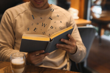 Wall Mural - Man with coffee reading book with letters flying over it at wooden table, closeup