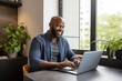 smiling adult black man working on a laptop at a table in a modern apartment