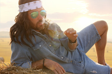 Canvas Print - Hippie man smoking joint on hay bale in field