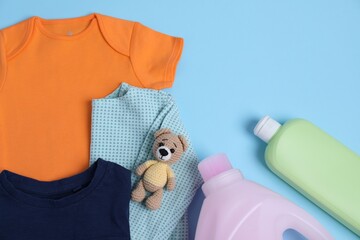 Canvas Print - Bottles of laundry detergents, baby clothes and toy bear on light blue background, flat lay. Space for text