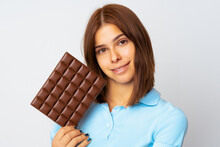 Girl With Chocolate. A Little Girl With Dark Short Hair In A Blue T-shirt Stands Smiling With A Large Chocolate Bar In Her Hand