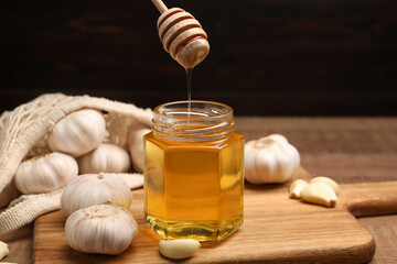 Wall Mural - Honey dripping from dipper into jar and garlic on table