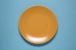 © New Africa - One orange ceramic plate on light blue background, top view