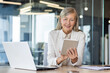 © Liubomir - Woman boss at workplace inside office, senior experienced gray-haired business woman uses tablet computer, happy checking financial data, banker finance woman with laptop.