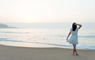 Wall Mural - Young asian woman relaxing on the beach at sunrise.