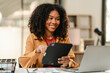 © Phushutter - smiling African American university student with an afro hairstyle, holding a tablet and sitting at a desk with a laptop. online class learning from video conference