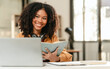 © makibestphoto - smiling African American university student with an afro hairstyle, holding a tablet and sitting at a desk with a laptop. online class learning from video conference