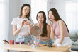 Beautiful three young Asian women doing makeup and testing lipsticks on together in living room. Korean or Japanese influencer girl with make up cosmetic routine at home. Makeup, friendship concept