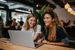 Two happy women using a laptop to brainstorm in a coworking space