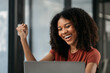 © NINENII - Excited african, american woman sitting at table feeling happy black woman overjoyed accepting mail at laptop promoted at home surprised girl reading good news.