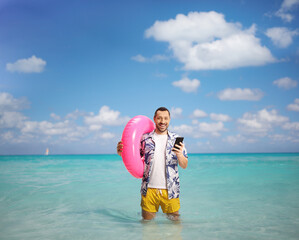 Wall Mural - Happy young man holding a swimming ring and a smartphone in the sea