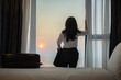 © shine - Businesswoman with suitcase opening the curtains and looking at the view from the window in luxury room of the expensive hotel after business meeting, Business trip, Booking hotel during your vacation