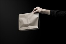 Person In A Dark Shirt Presents A Paper Bag, Poised To Reveal Its Contents Against A Deep Black Background, Creating An Aura Of Anticipation