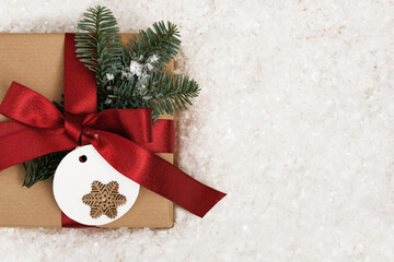 Wall Mural - Card with gift box with fir tree sprig and label with snowflake on snow background. Space for your text.