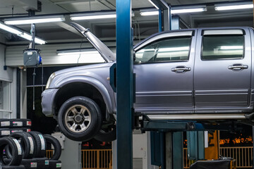 Pickup truck lifted into the air using a mechanical bridge jack in a service garage for car repair and maintenance at night time