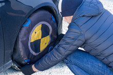 Man putting textile snow chains on the car wheel. Safety on winter travels.