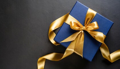 Poster - dark blue gift box with gold satin ribbon on dark background top view of birthday gift with copy space for holiday or christmas present