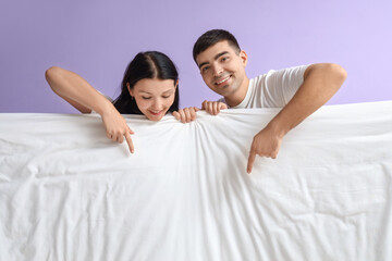 Wall Mural - Young couple with blanket pointing at something on lilac background