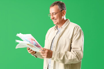 Wall Mural - Mature man in eyeglasses reading newspaper on green background