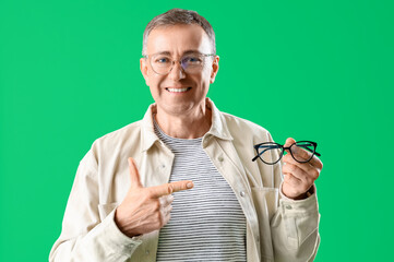 Canvas Print - Mature man pointing at eyeglasses on green background