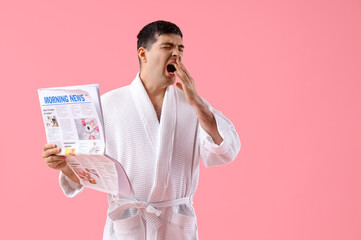 Poster - Handsome young man in bathrobe with newspaper on pink background