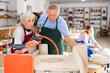 © JackF - Elderly potter teaches a woman how to roll clay on a craft machine clay press roller