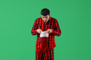 Sticker - Young man in pajamas with Santa sock on green background