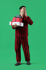 Sticker - Young man in pajamas with Christmas gift boxes on green background