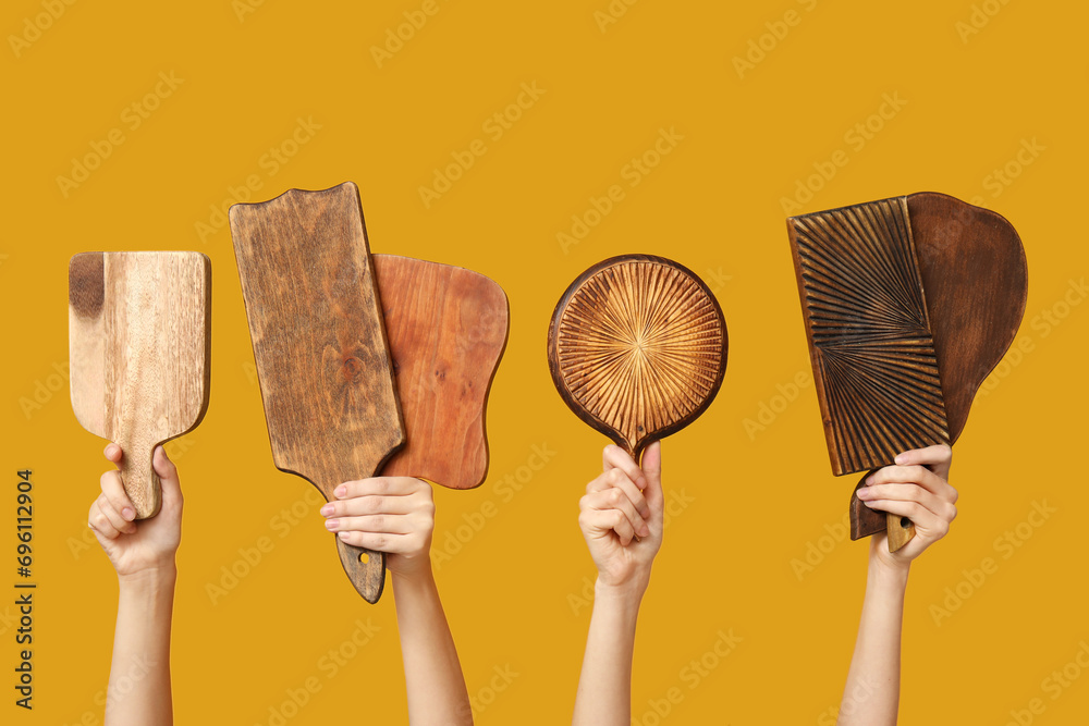 Female hands with wooden cutting boards on yellow background
