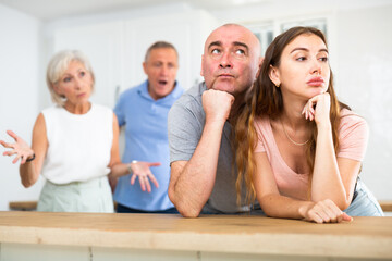 Wall Mural - Portrait of an offended married couple in a home kitchen, which mature family members reprimand. Family conflict