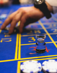 Wall Mural - Vibrant casino table with roulette in motion, with casino chips, tokens, the hand of croupier, dollar money and a group of gambling rich people playing bet, blue poker table and deck of cards