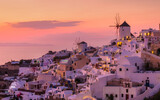 Fototapeta Uliczki - Oia village, Santorini, Greece. View of traditional houses in Santorini. Small narrow streets and rooftops of houses, churches and hotels. Landscape during sunset. Travel and vacation photography.