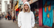 Young woman wearing a blank white hoodie standing with her hands in pocket, smiling, looking at camera, sweatshirt apparel mockup, Graffiti street background, teenage fashion, mock-up photo