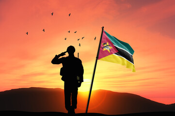 Silhouette of a soldier with the Mozambique flag stands against the background of a sunset or sunrise. Concept of national holidays. Commemoration Day.